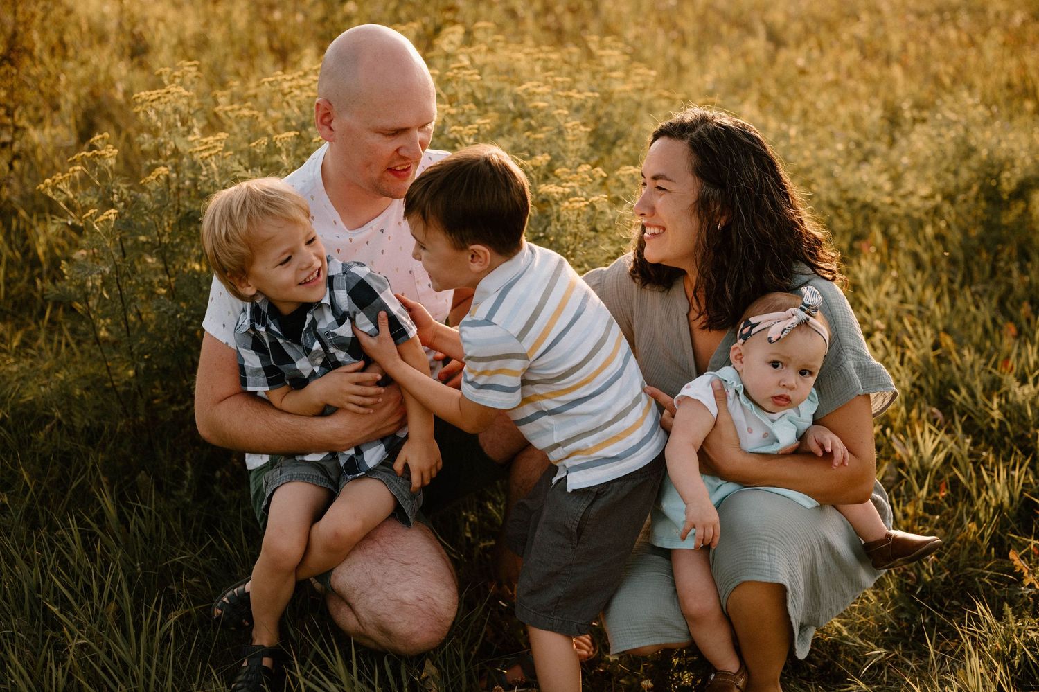 Joyful family of five laughing together in a sun-drenched grassy meadow.