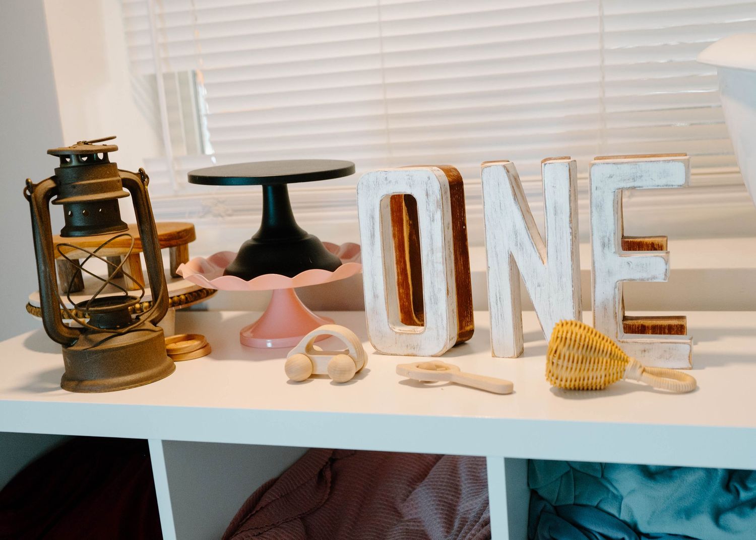 Photography prop shelf displaying a brass lantern, cake stands, letter ONE sign, and wooden toys.