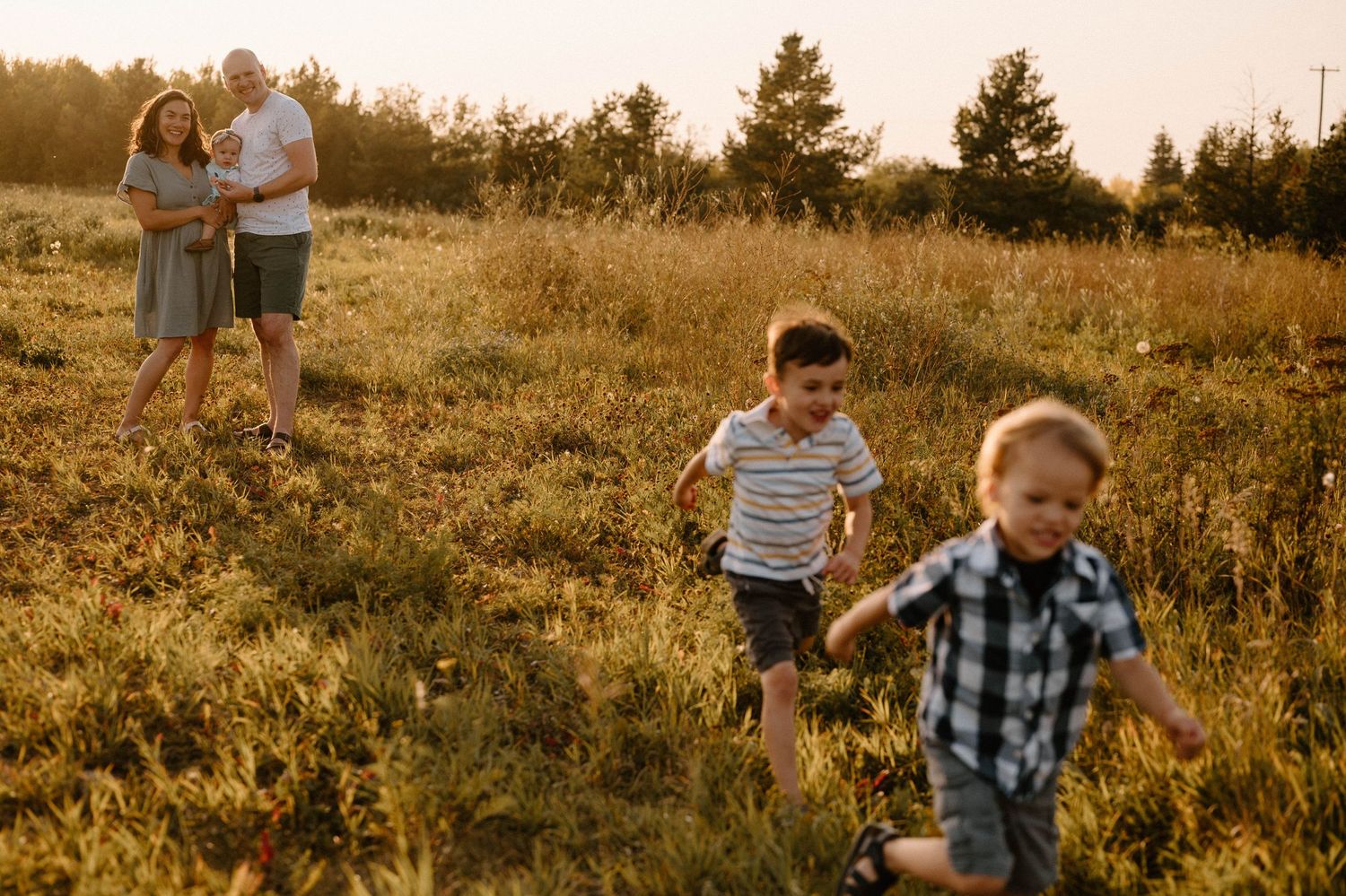Family with two young boys running through a golden sunlit field during an outdoor photo session.