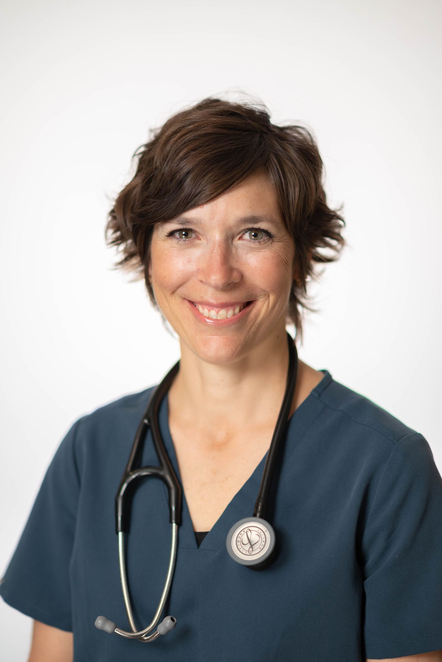 Female healthcare professional in teal scrubs smiling with stethoscope around neck.