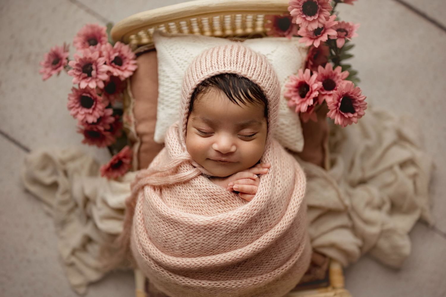 Baby girl wrapped in pink on a boho bead with pink flowers and a bonnet