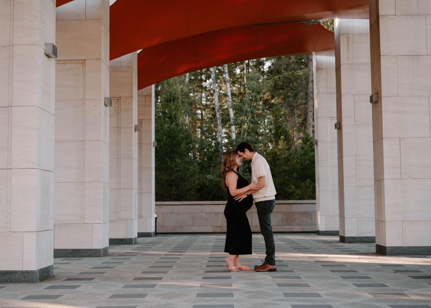 Couple sharing a romantic moment under a red architectural arch at UOA Botanical Gardens.