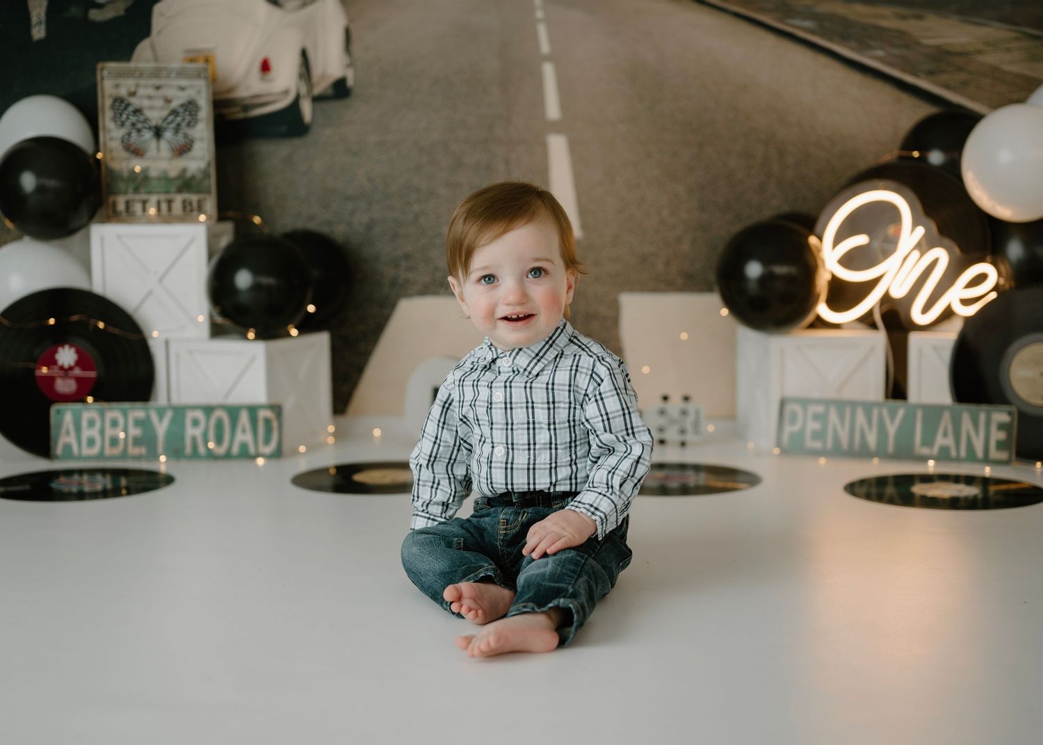 Happy red-haired toddler sits before Beatles Abbey Road Penny Lane themed first birthday party decorations.