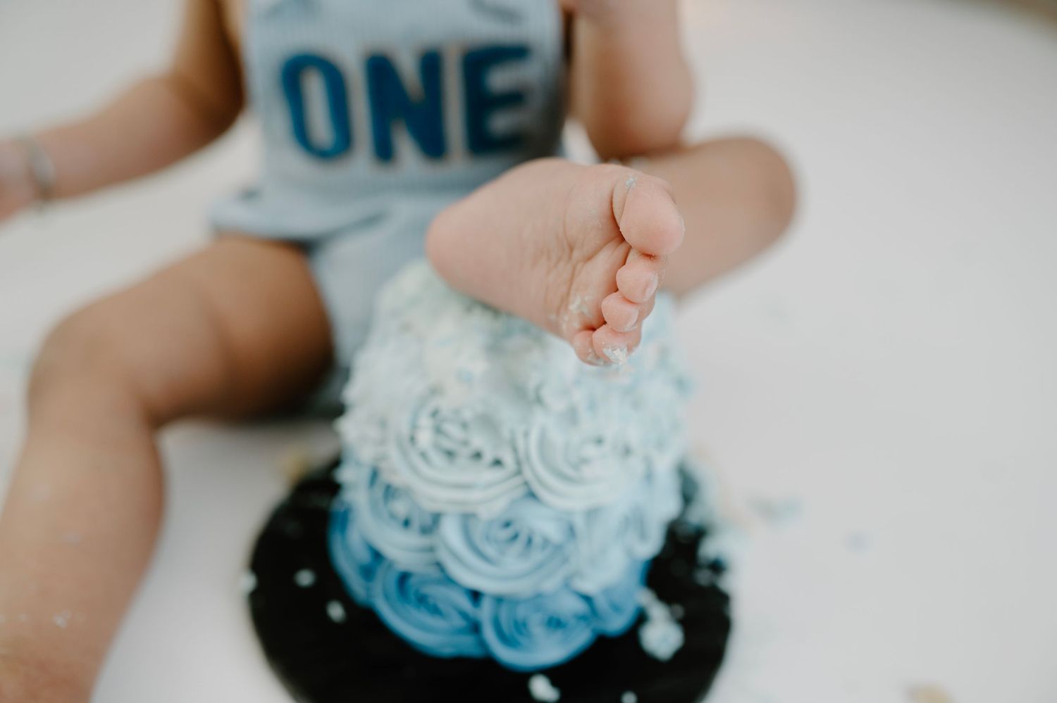 A baby's hand smashing into a blue ombre rosette birthday cake during a first birthday cake smash.