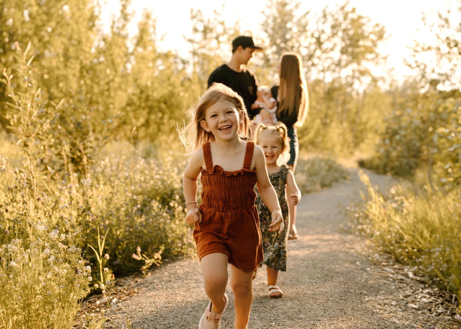 Young girl laughing and running on a Telford Lake walking path with family walking behind in golden light.