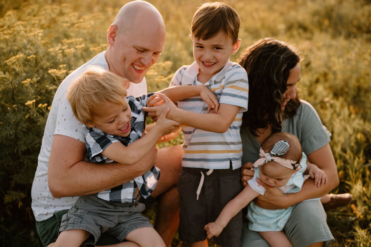 Cheerful family of five sharing a playful moment in a golden wildflower field.