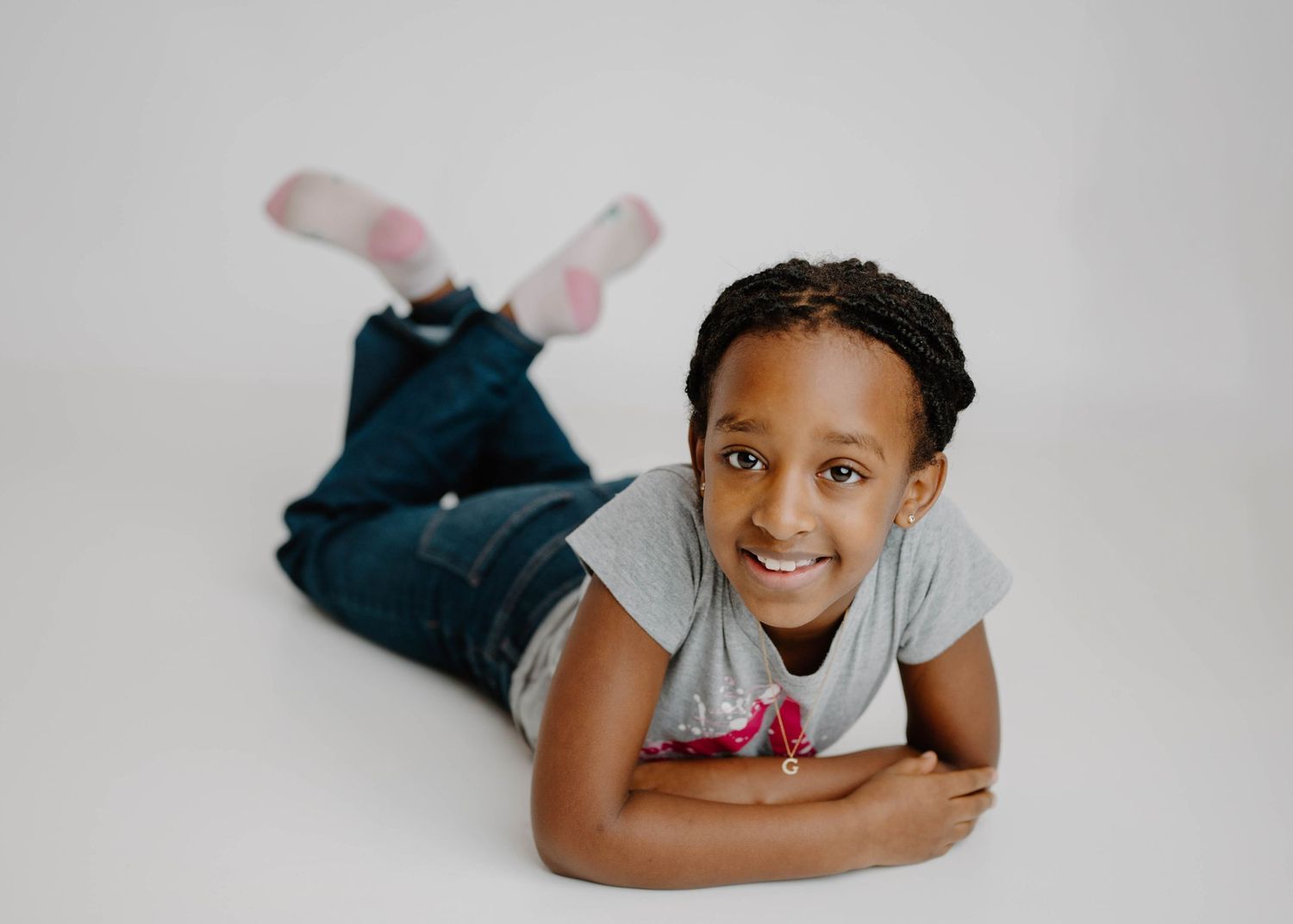 Happy young girl lying on white studio floor wearing gray tee and jeans with pink socks.