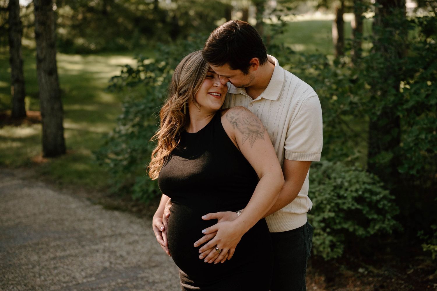 Couple shares intimate moment on garden path as man embraces pregnant partner from behind at dusk.