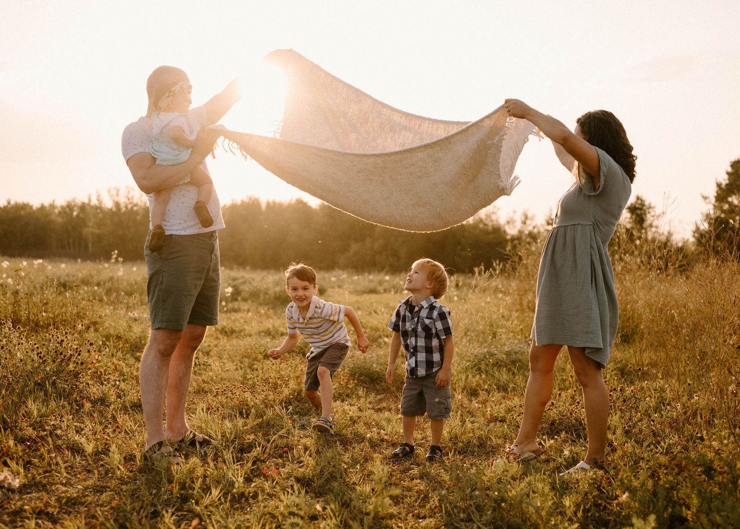 Family of five enjoying playful moment with a blanket in a sunlit field during golden hour.