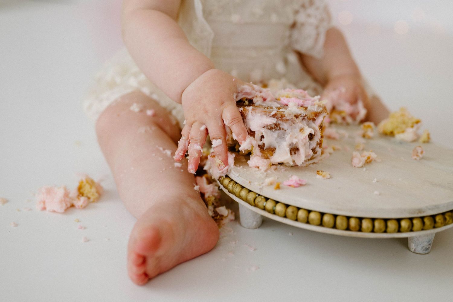 Close-up of baby hands smashing pink and white first birthday cake on marble and gold cake stand.