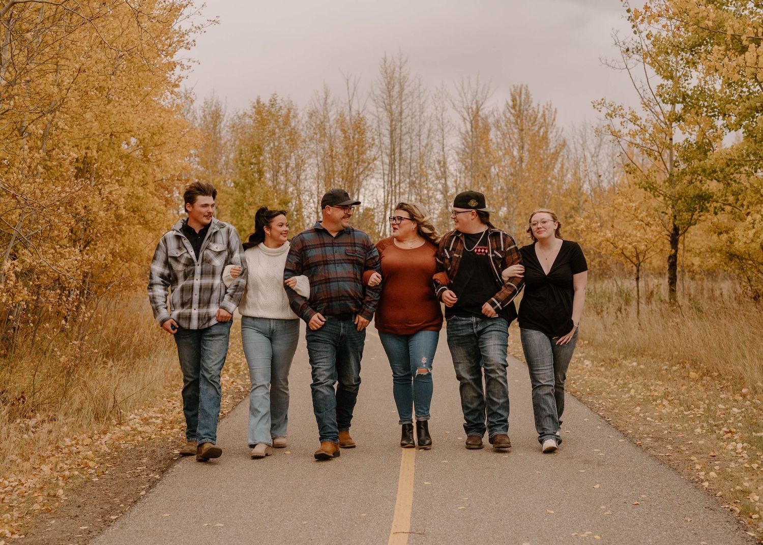 Group of six adults walking together on a tree-lined road surrounded by vibrant fall foliage.