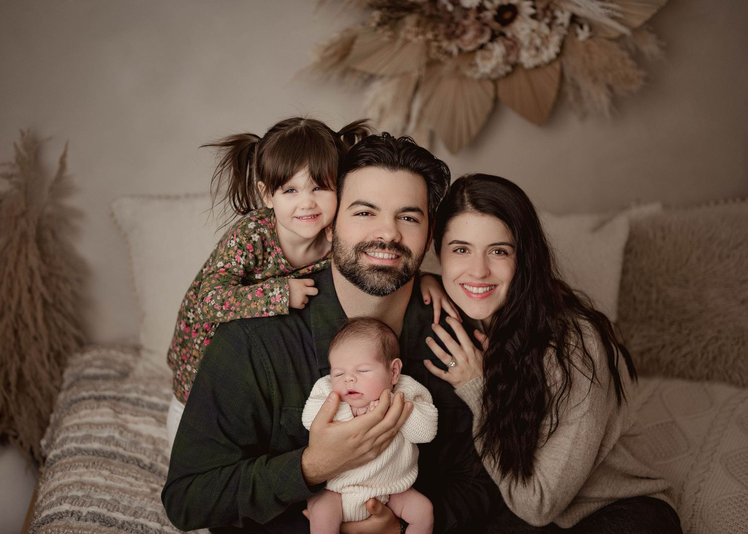 Family photo of a mom dad baby and older sister on a boho backdrop in a studio In Leduc Alberta