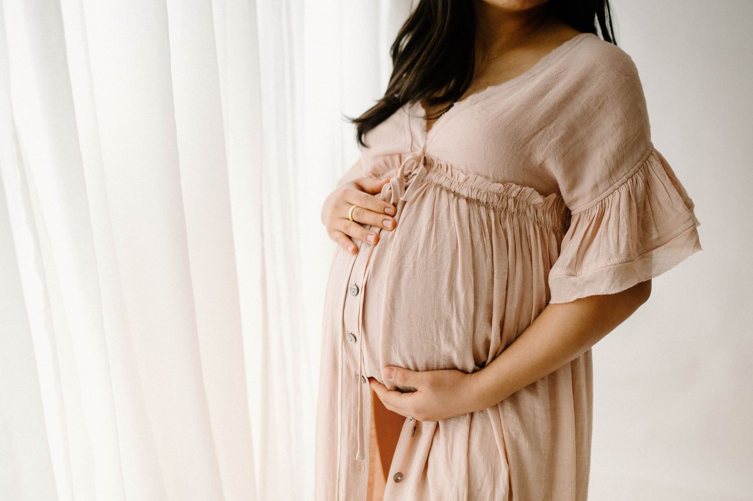 Close-up of pregnant woman in blush ruffled dress gently cradling her baby bump.