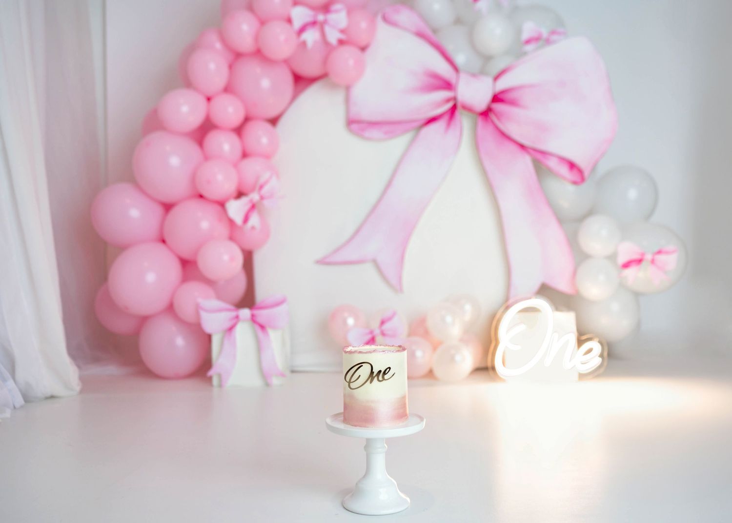 Elegant pink bow and balloon arch first birthday cake smash setup with One sign decor.