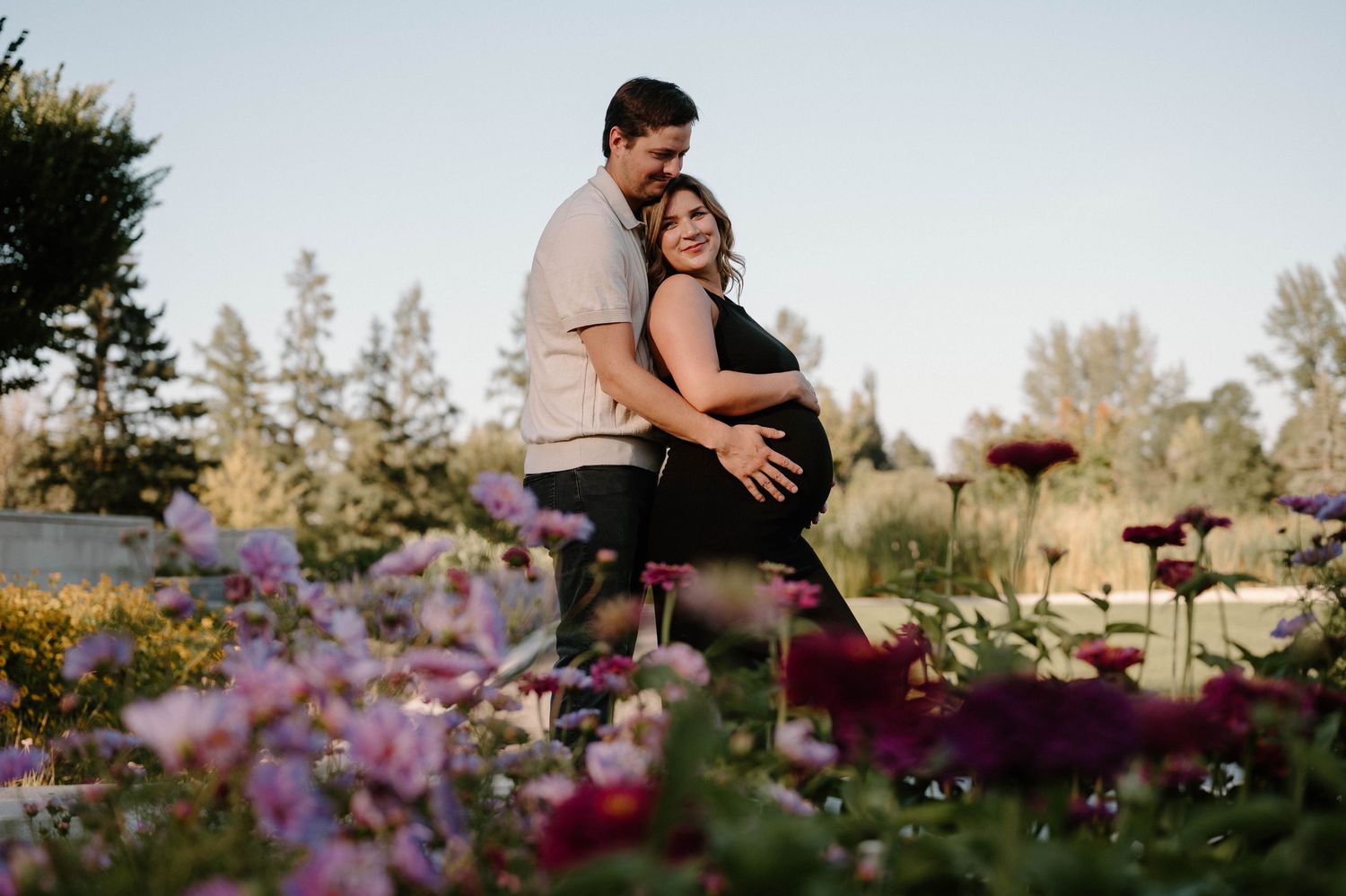 Expecting couple embracing in a garden surrounded by colorful blooming flowers at sunset.
