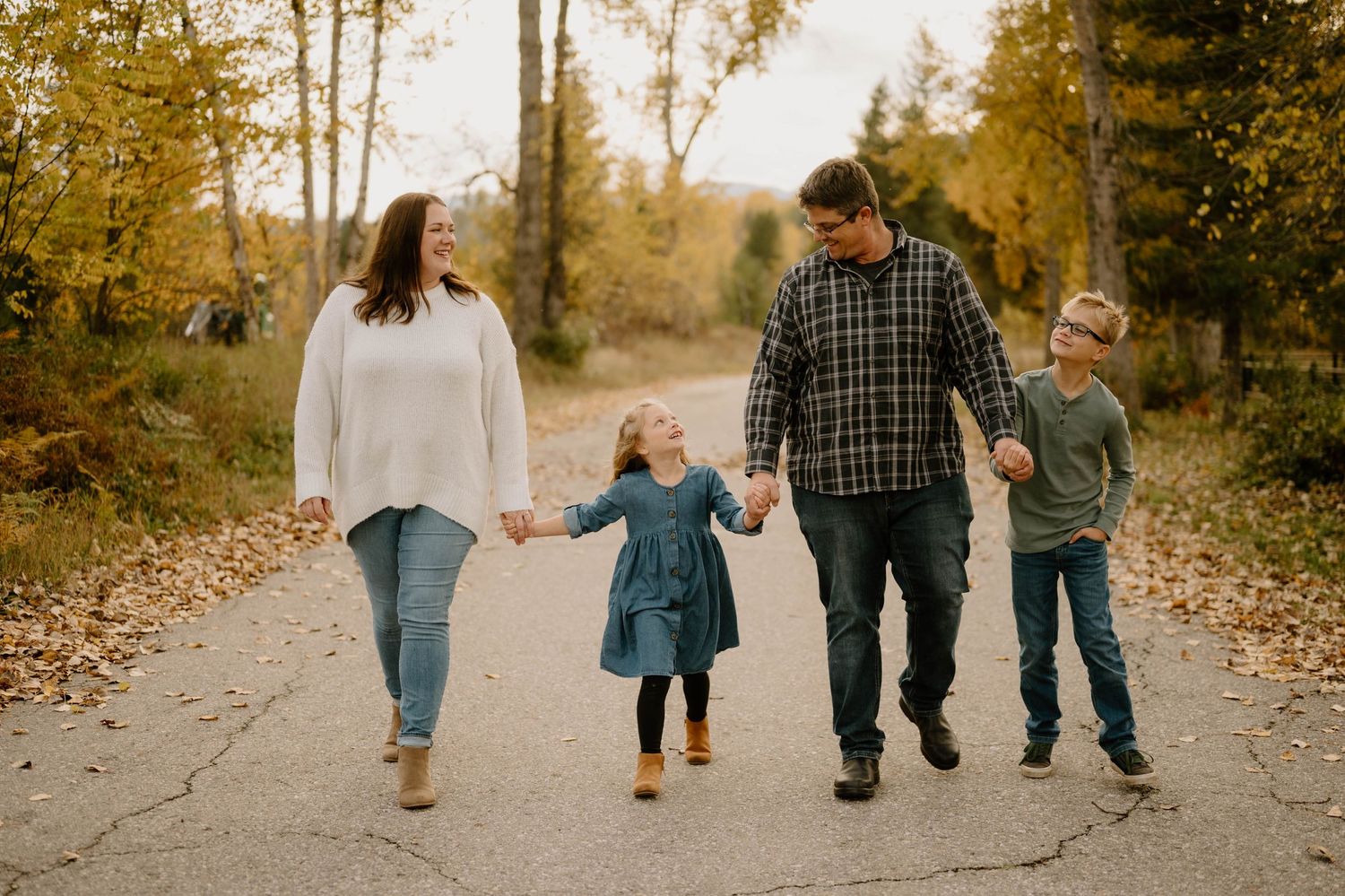 A happy family of four walks hand-in-hand along a scenic autumn pathway.