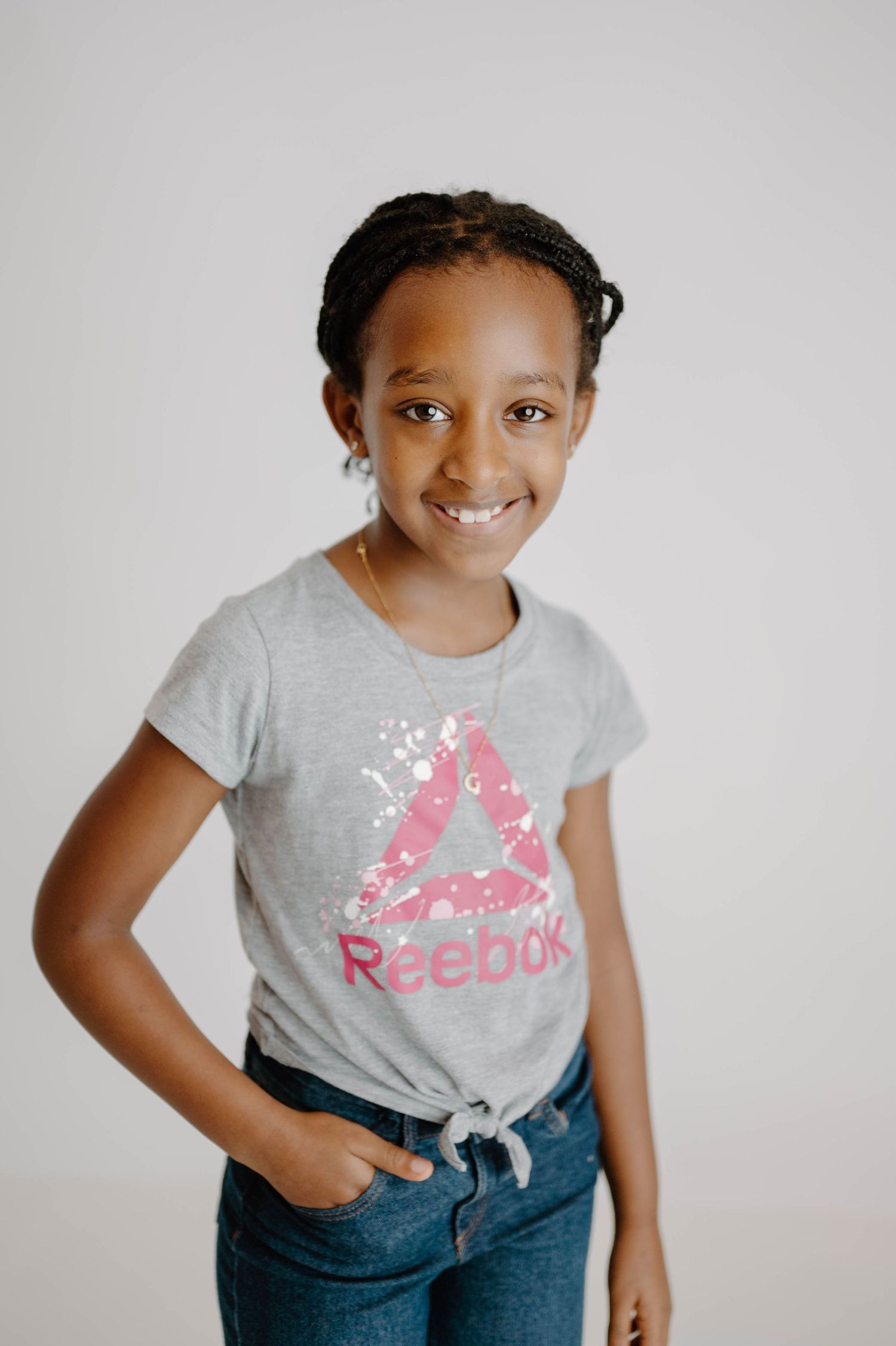 Young Black girl in a gray Reebok t-shirt and jeans smiling with hand in pocket.