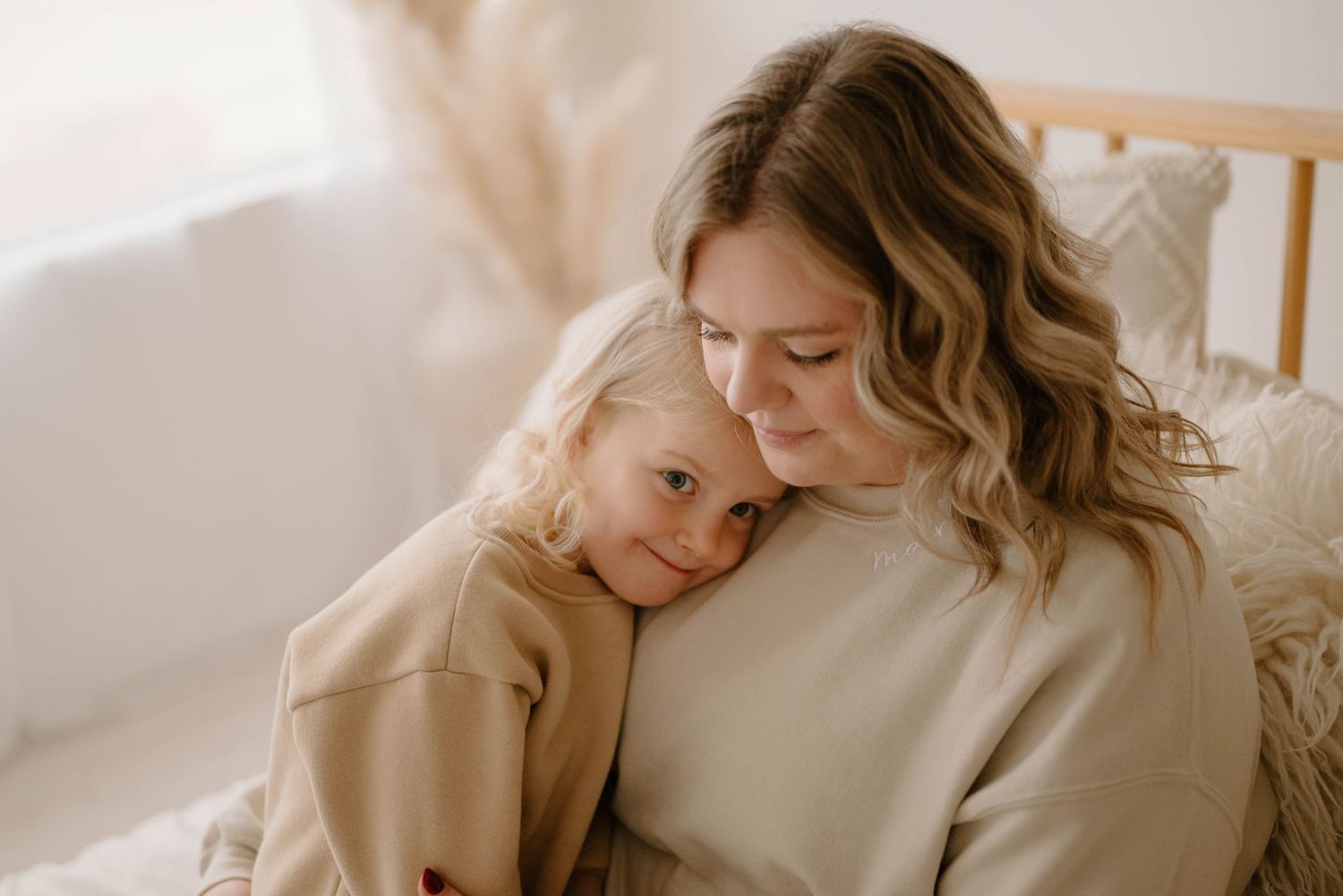 Mother and young daughter sharing a tender embrace while sitting together in a softly lit room.