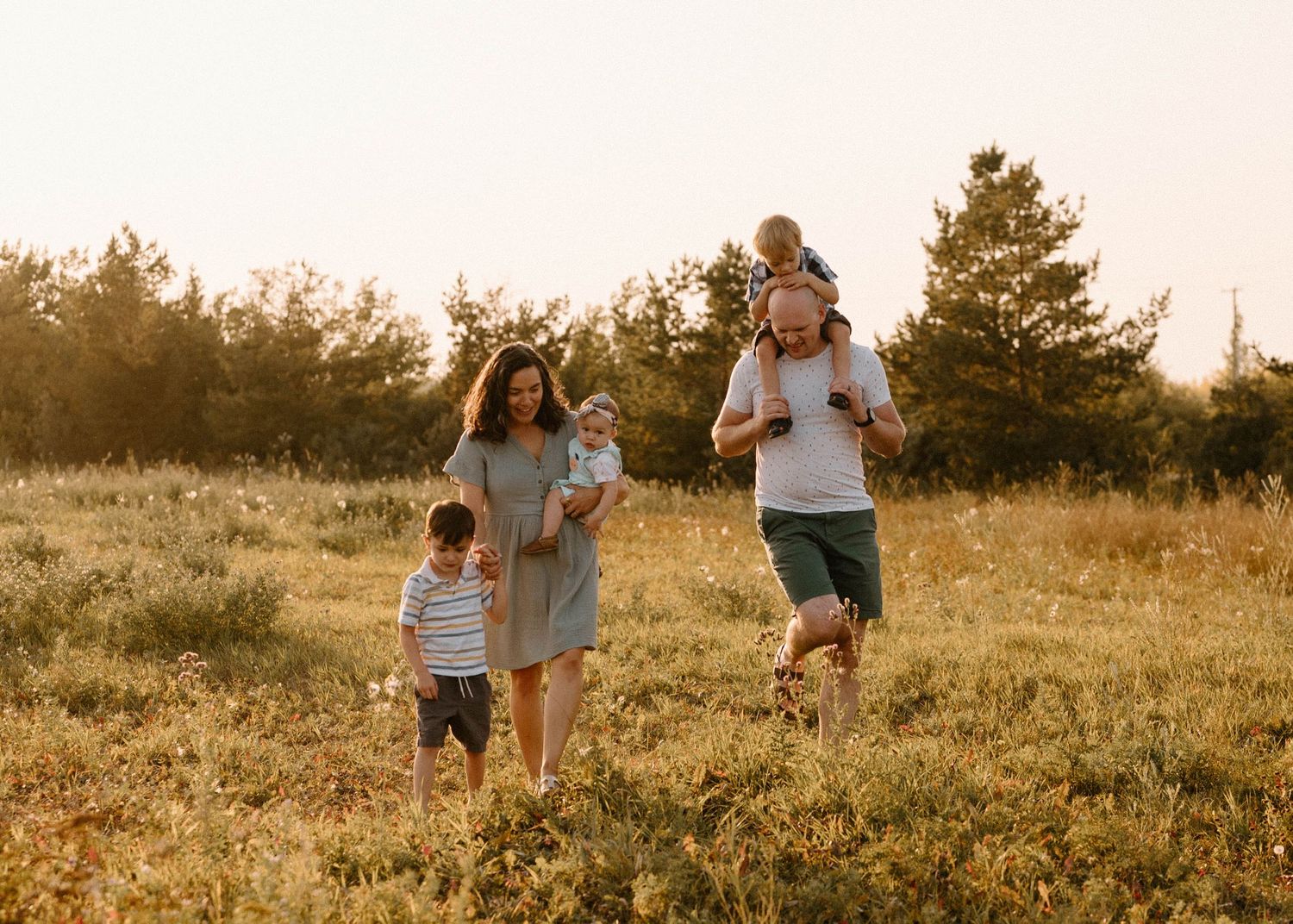Happy family of five walking through a golden sunlit meadow at sunset.