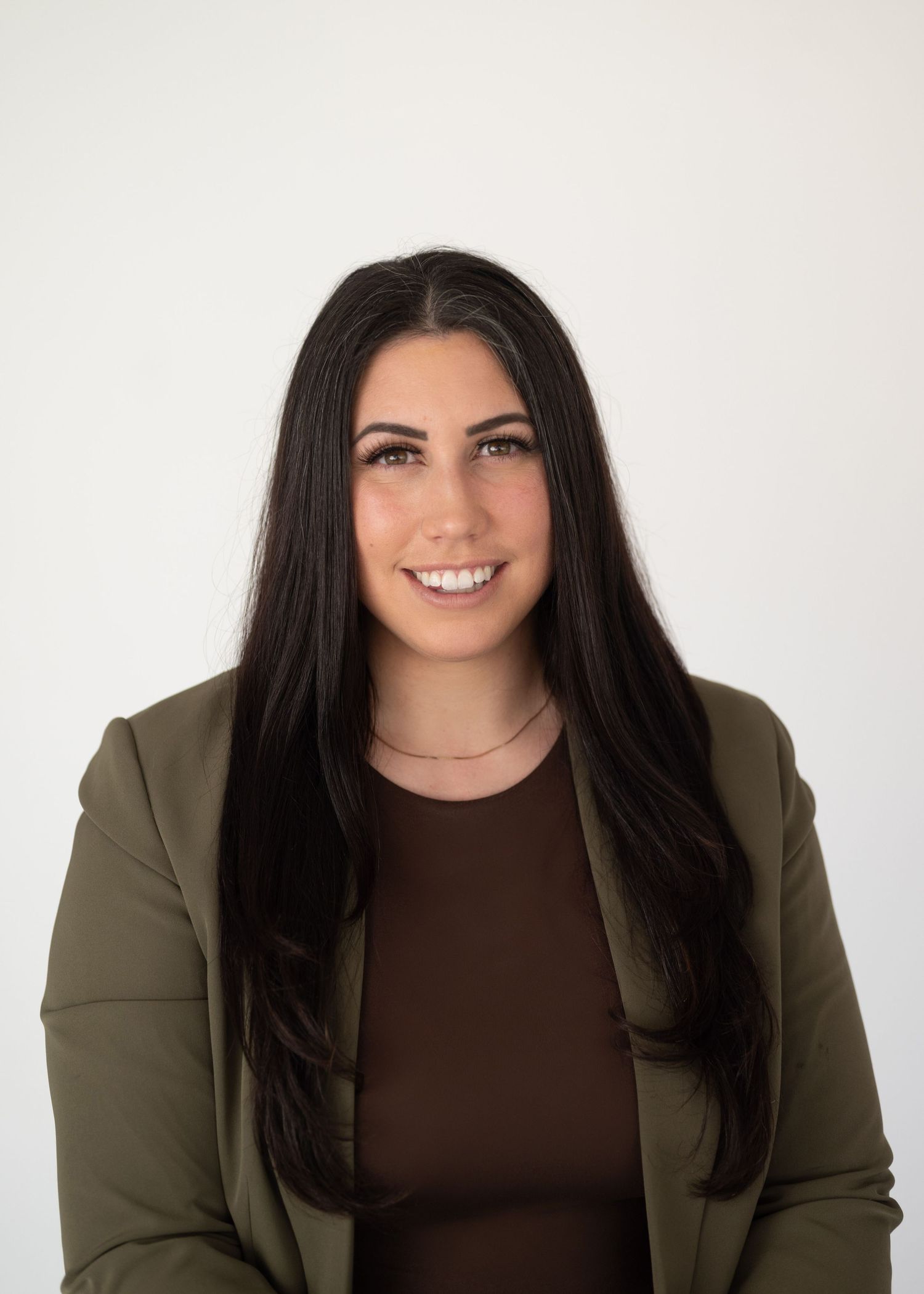 Professional woman with long black hair smiling in an olive blazer against a white background.