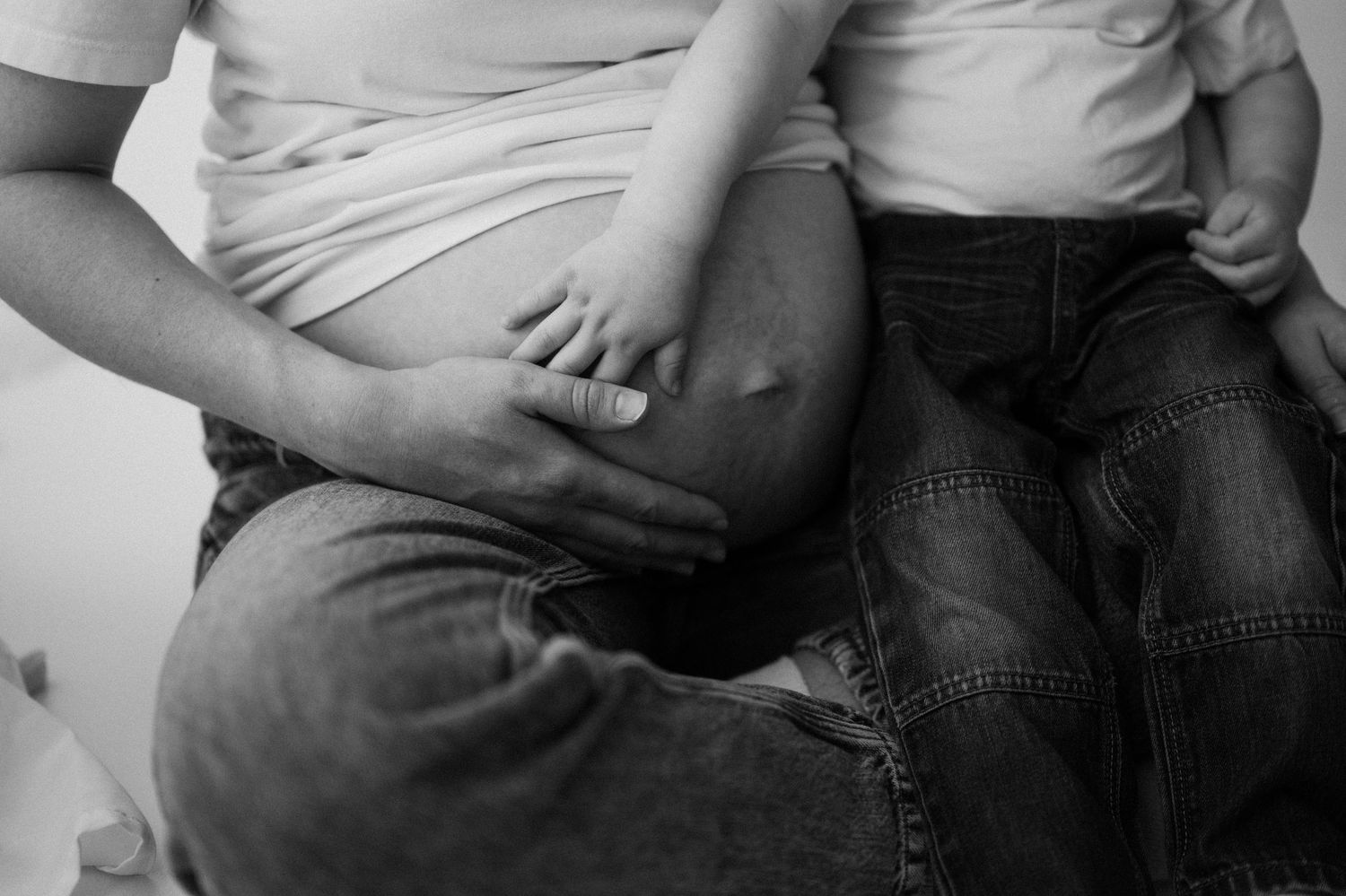 Black and white close-up of a pregnant woman sitting with a young child touching her baby bump.