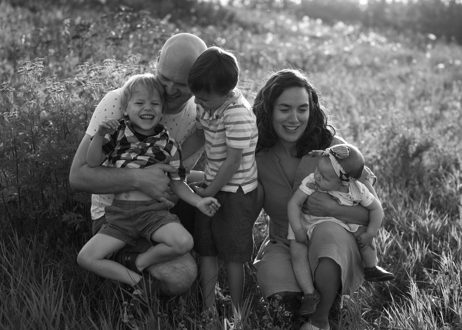 Black and white family photo of parents with three young children in a meadow.