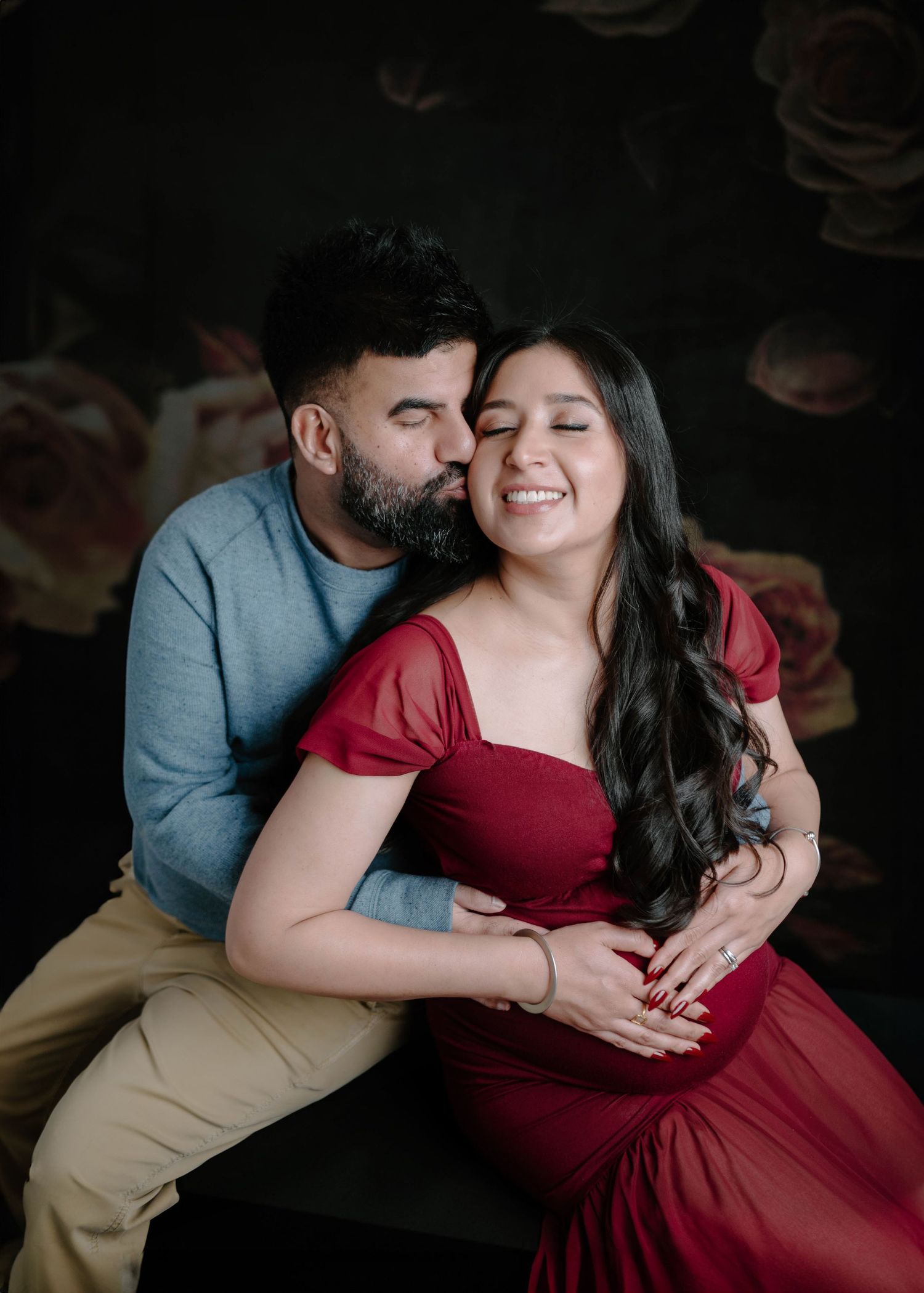 Couple sharing tender moment, man kissing pregnant woman's cheek, both holding baby bump.