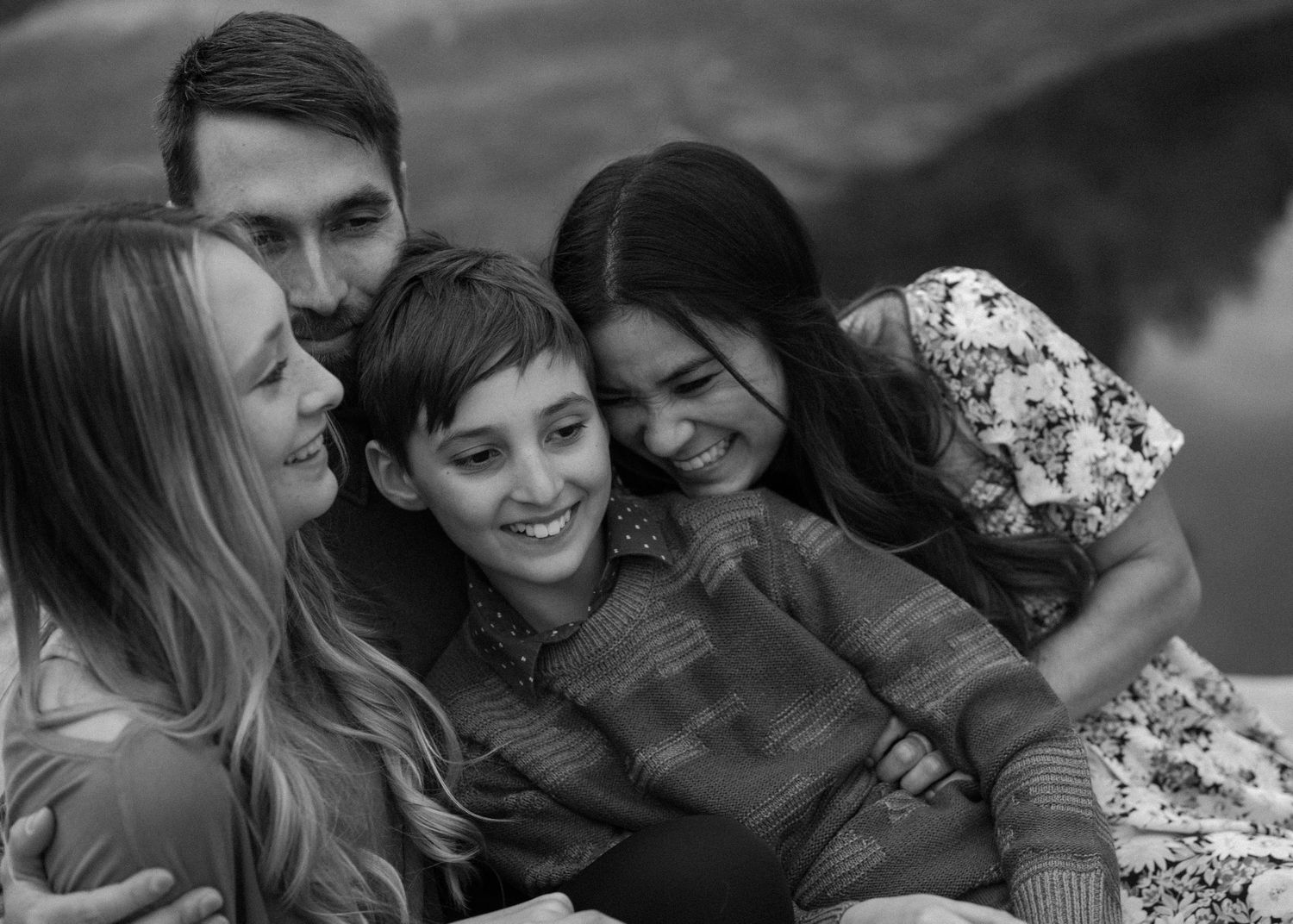 Black and white photo of a joyful family of four hugging and laughing closely together.