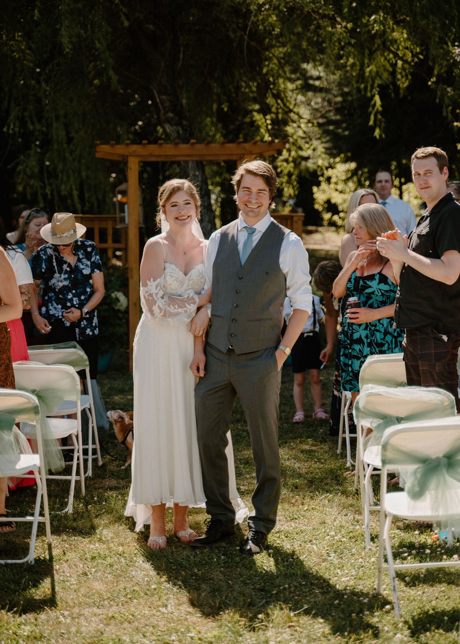 Newlyweds walk joyfully down the aisle after outdoor ceremony surrounded by applauding wedding guests.