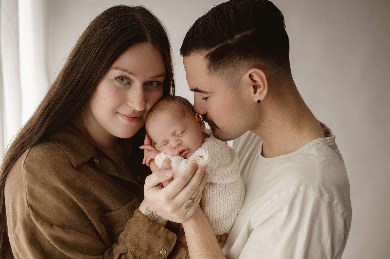 Parents tenderly holding sleeping newborn baby between them in warm and cozy Leduc Studio.