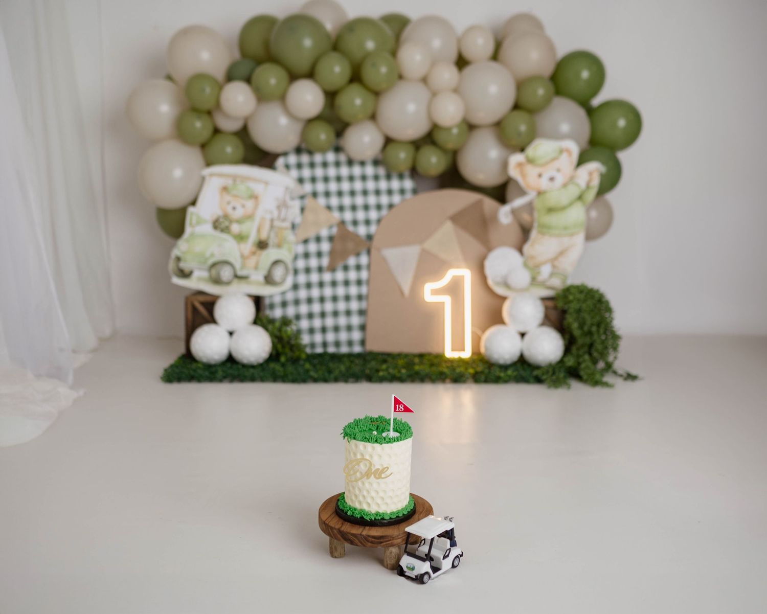 Golf themed first birthday cake smash setup with green and beige balloon garland, number one candle, and mini golf cart.