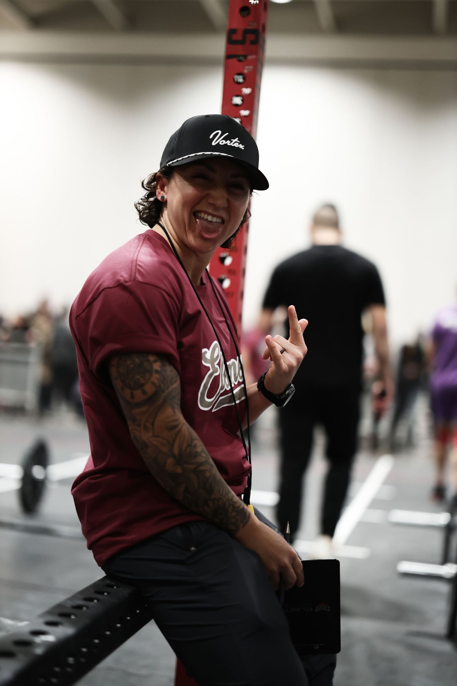 Person in a black cap and burgundy shirt laughing while sitting in a casual indoor setting.
