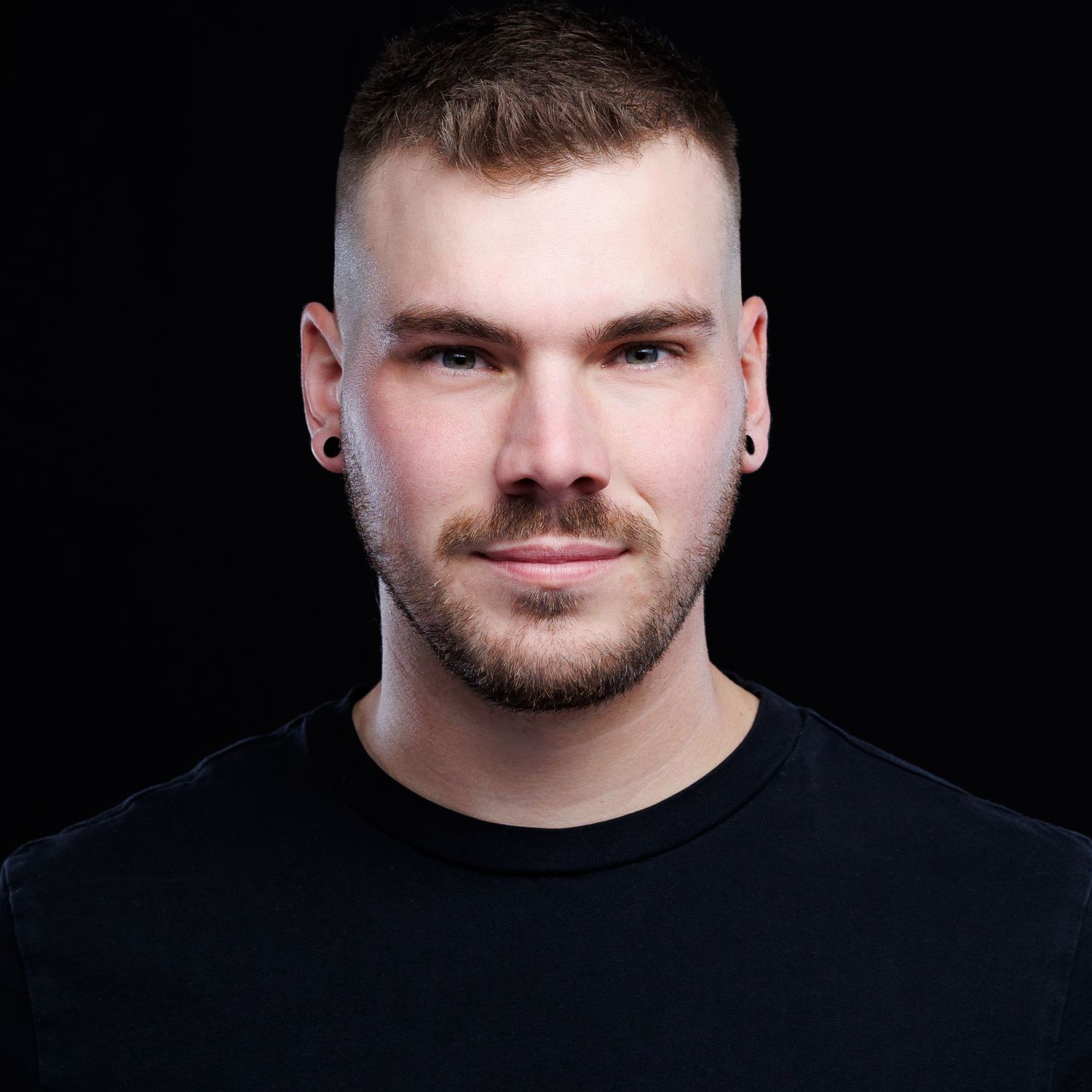 Studio portrait with dramatic lighting shot against black background showcasing short hairstyle and facial features.