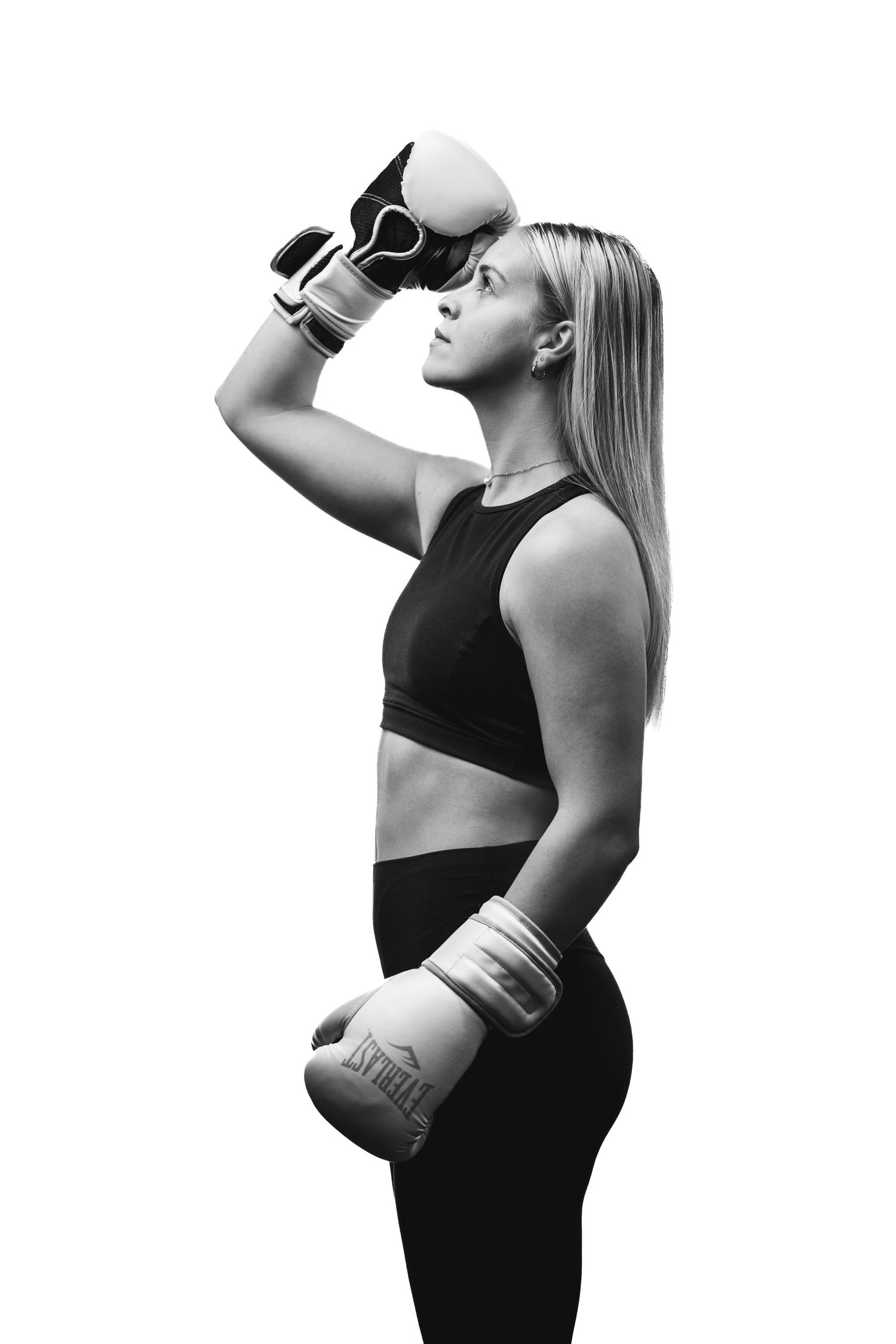 Black and white image of a boxer in workout attire holding gloves and standing in profile against white background.