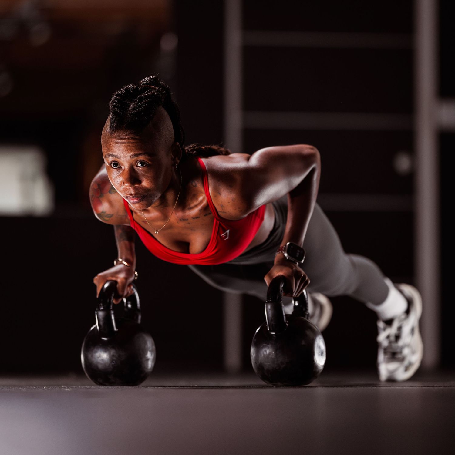 Strong athlete performs push-ups on kettlebells during an intense workout session in a dark gym setting.