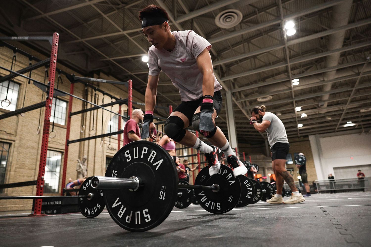A person performs a deadlift exercise with a barbell in a dimly lit industrial gym setting.