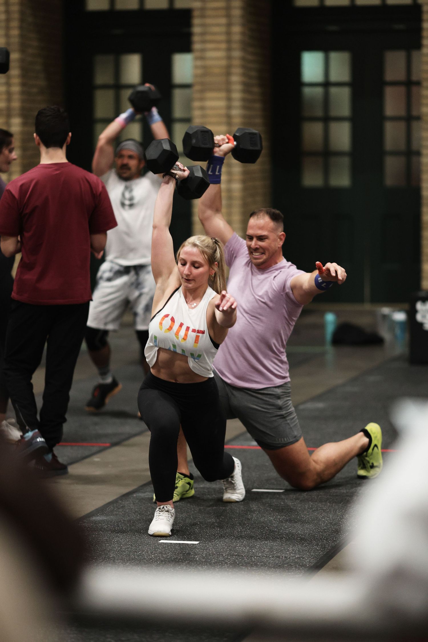 Group fitness class participants doing lunges with weights in an indoor gym setting.