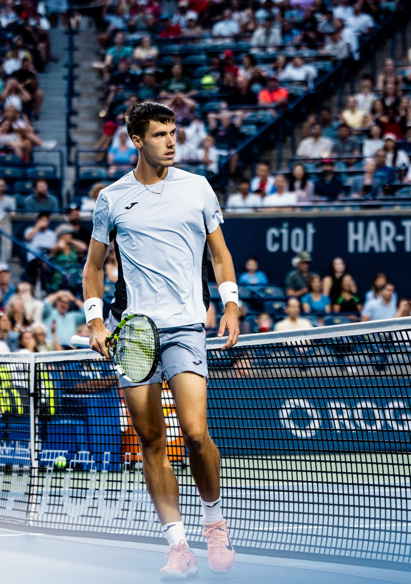 Tennis player in white attire performs a low volley shot at the net during a professional match.