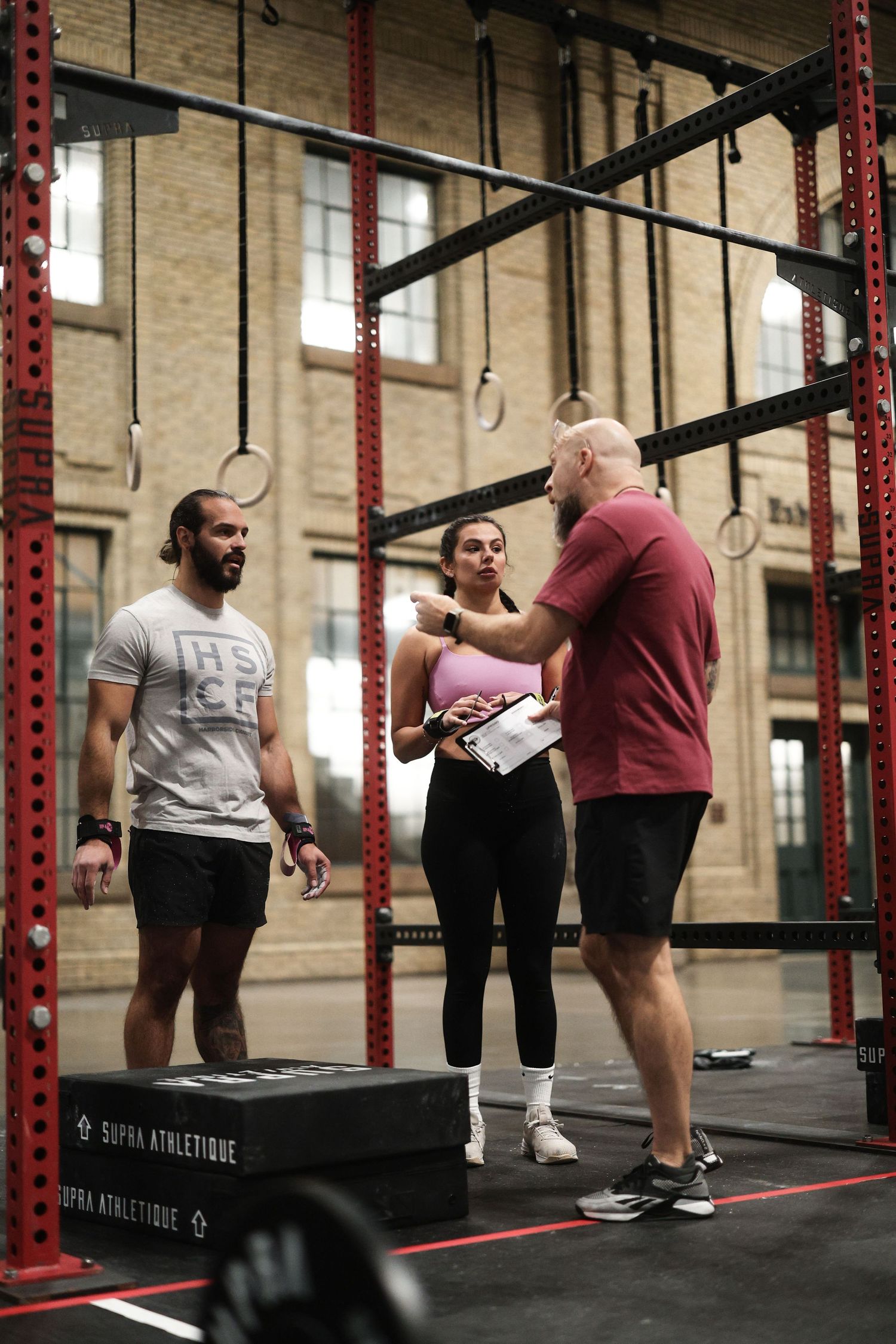 Group of people exercising and stretching in a CrossFit style gym with red support beams and brick walls.