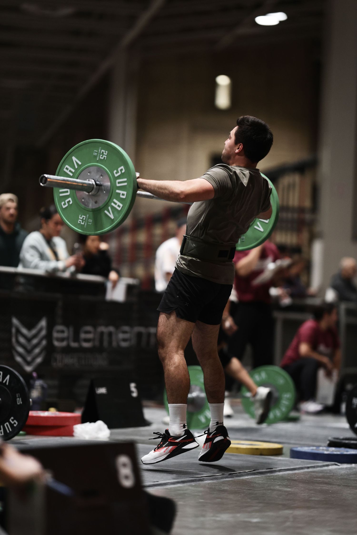 Athletes perform Olympic weightlifting movements with green-plated barbells in a dark indoor gym setting.