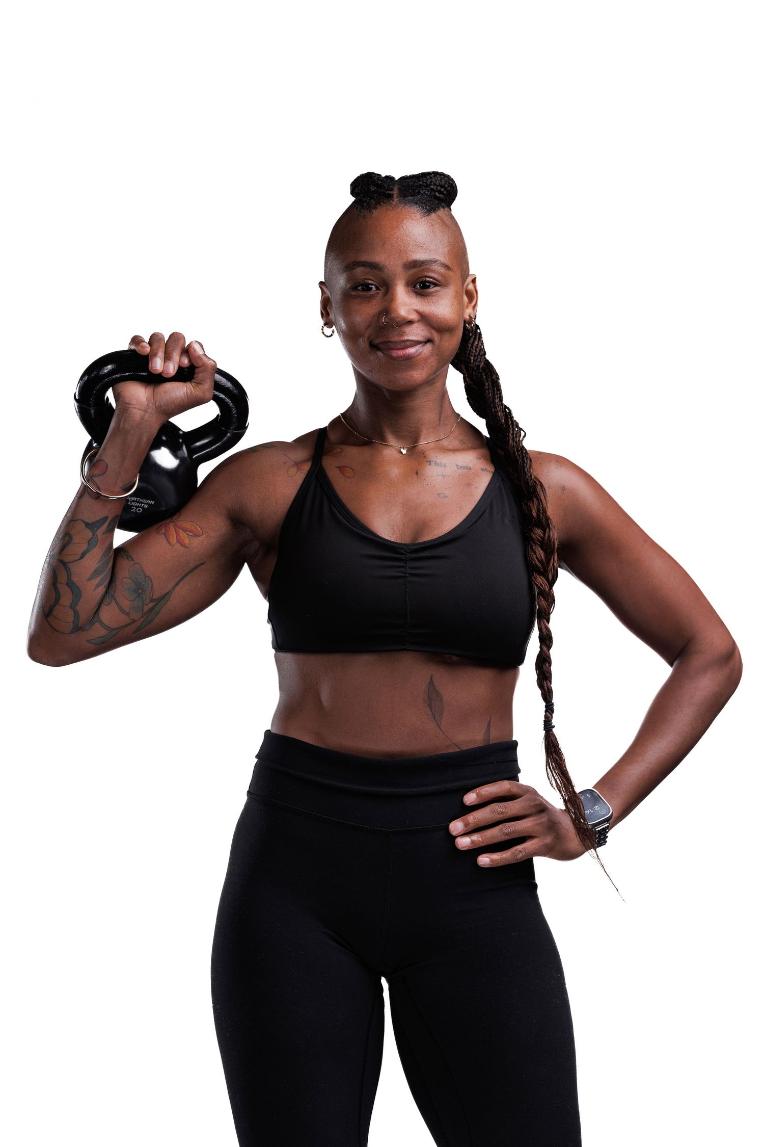Athletic person in black workout attire holds a kettlebell while posing confidently against white background.