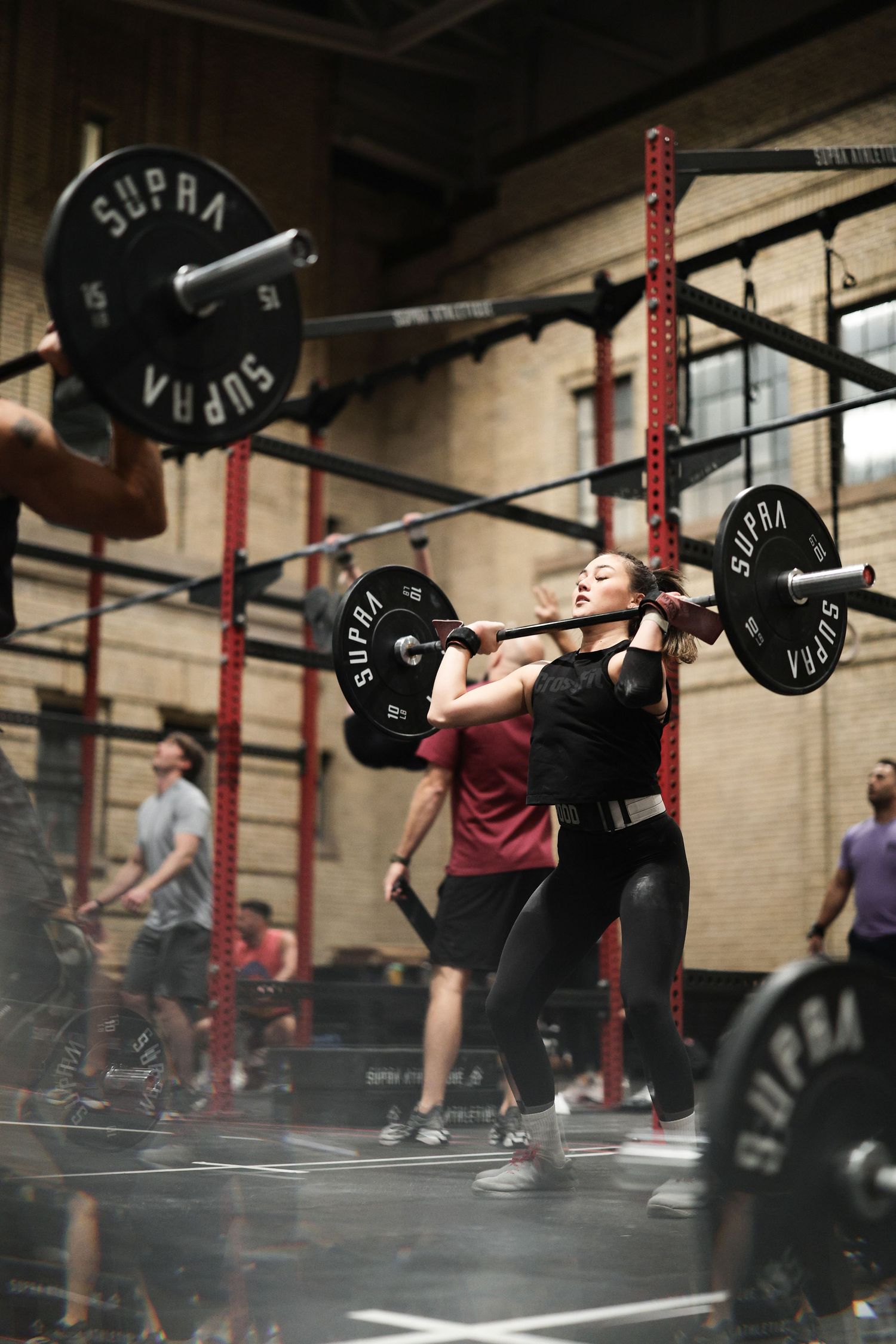A sequence of weightlifting movements showing an athlete performing an overhead snatch in a CrossFit gym setting.