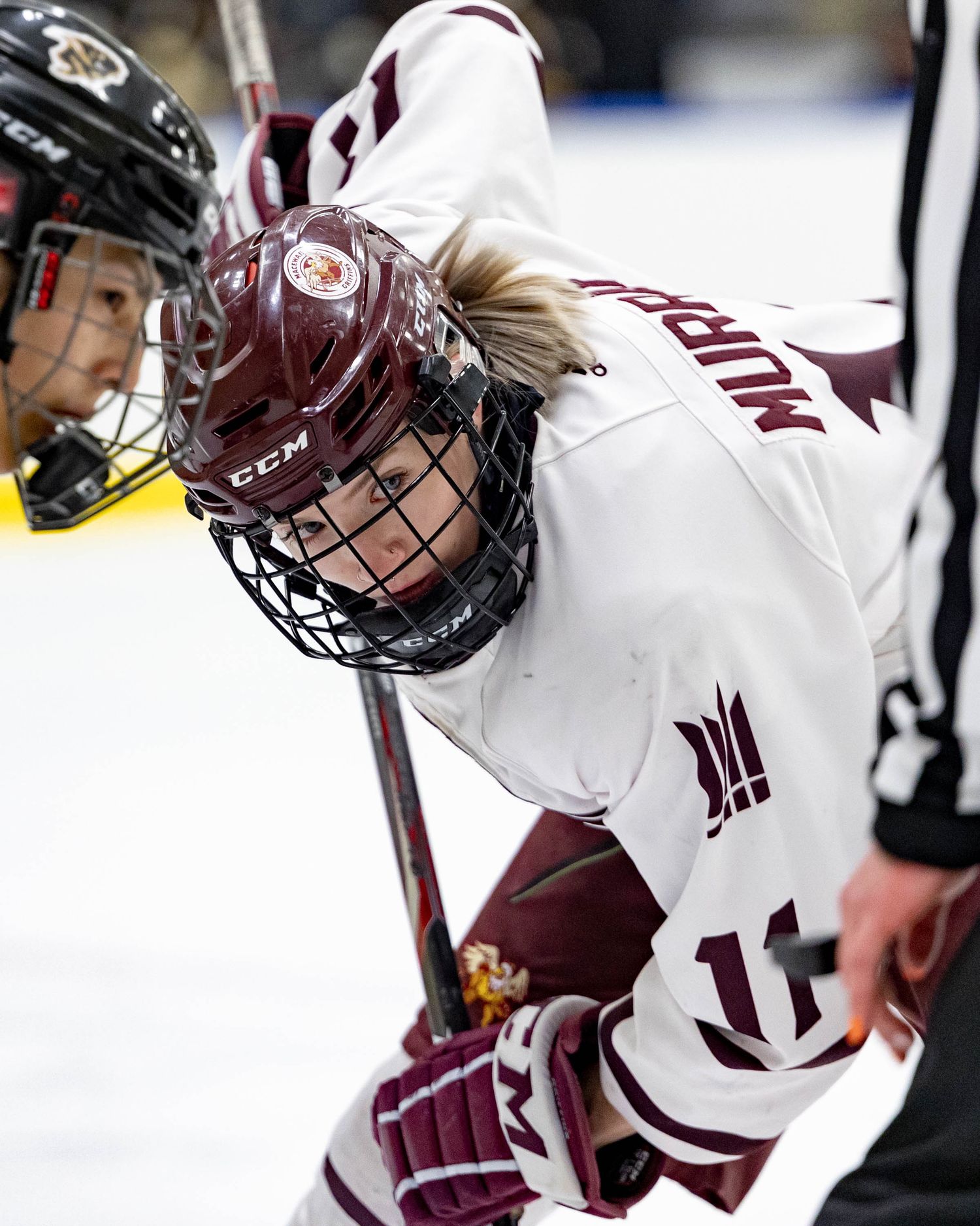 Ice hockey player in maroon and white uniform leans forward during face-off at a competitive match.