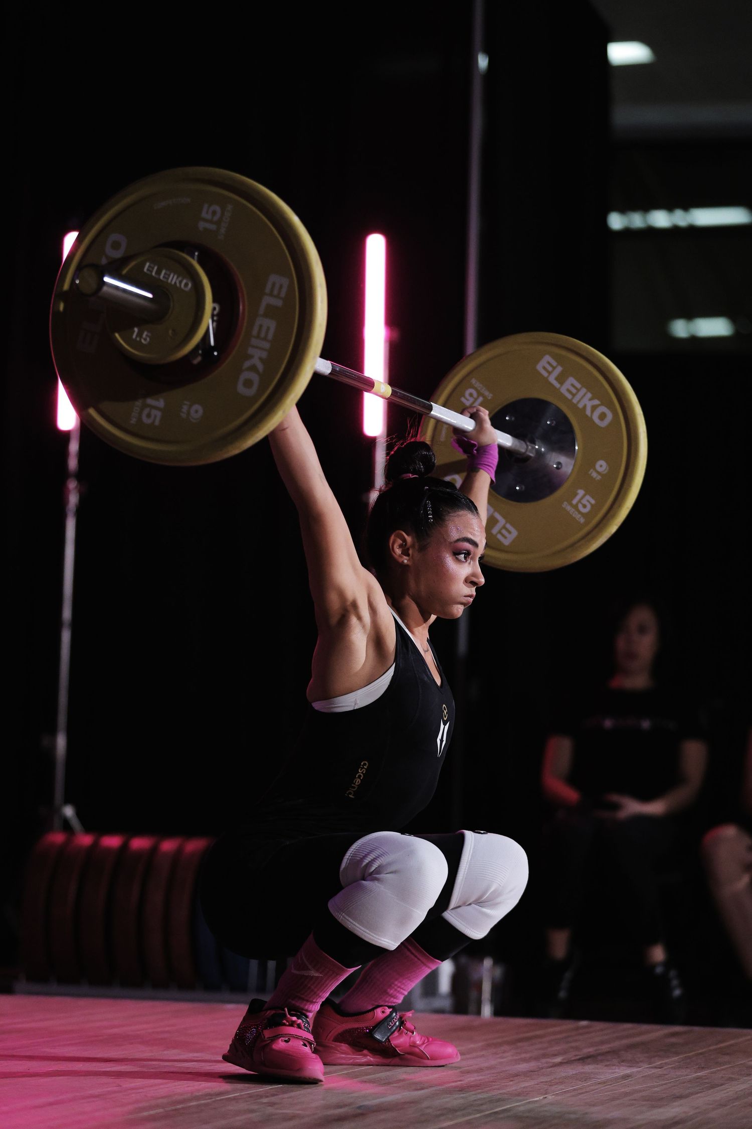 An athlete performs an Olympic weightlifting snatch sequence against a dark background with pink lighting accents.