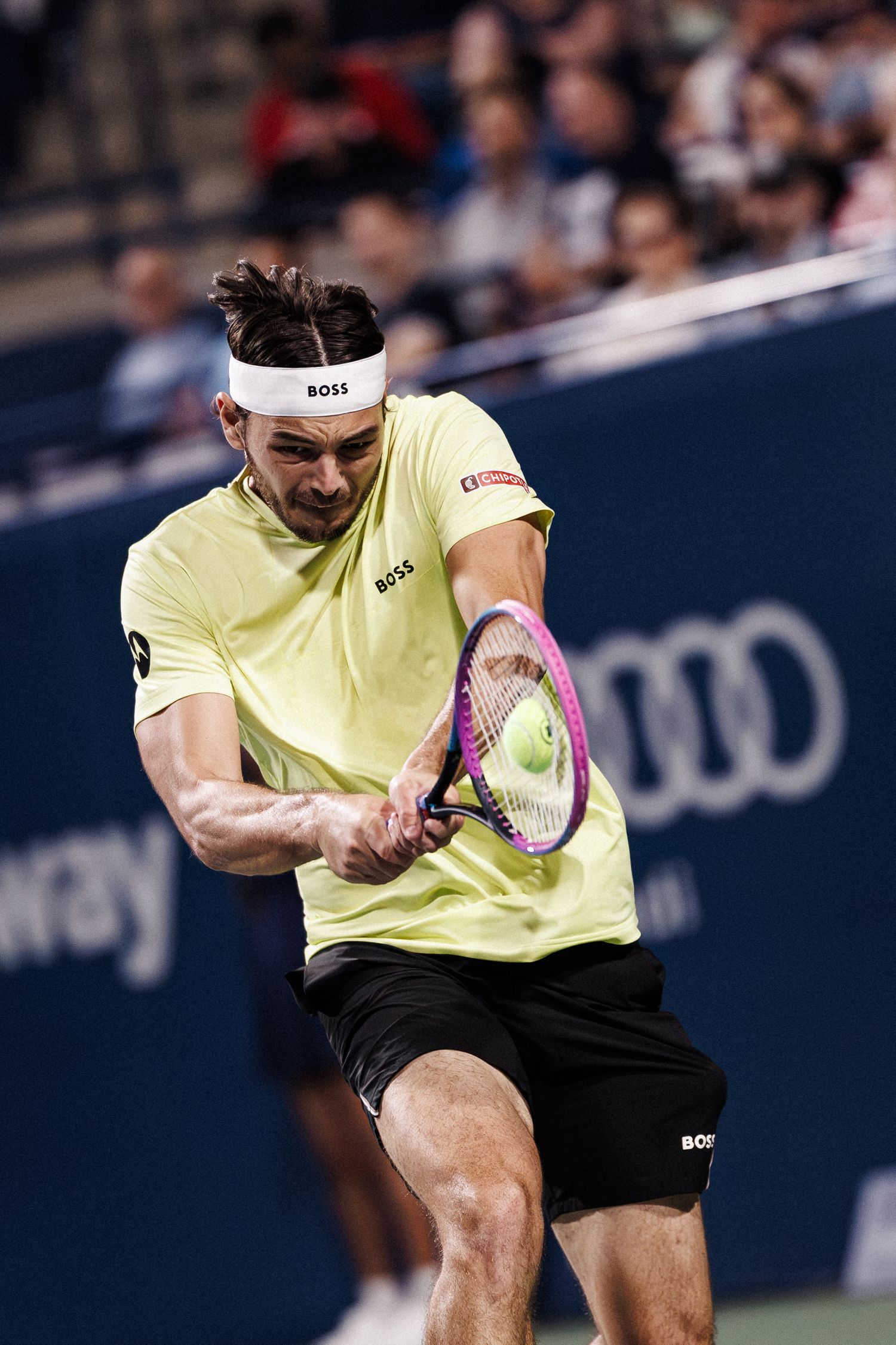 Tennis player in yellow shirt and black shorts hits a powerful forehand shot during a professional match.