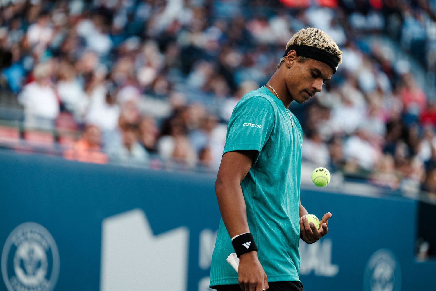 Tennis player in turquoise shirt serves the ball during a professional match on outdoor court.