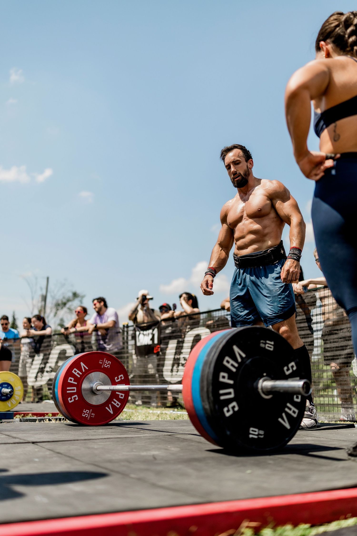 Athletes perform Olympic weightlifting deadlifts with red and blue plates during an outdoor competition event.