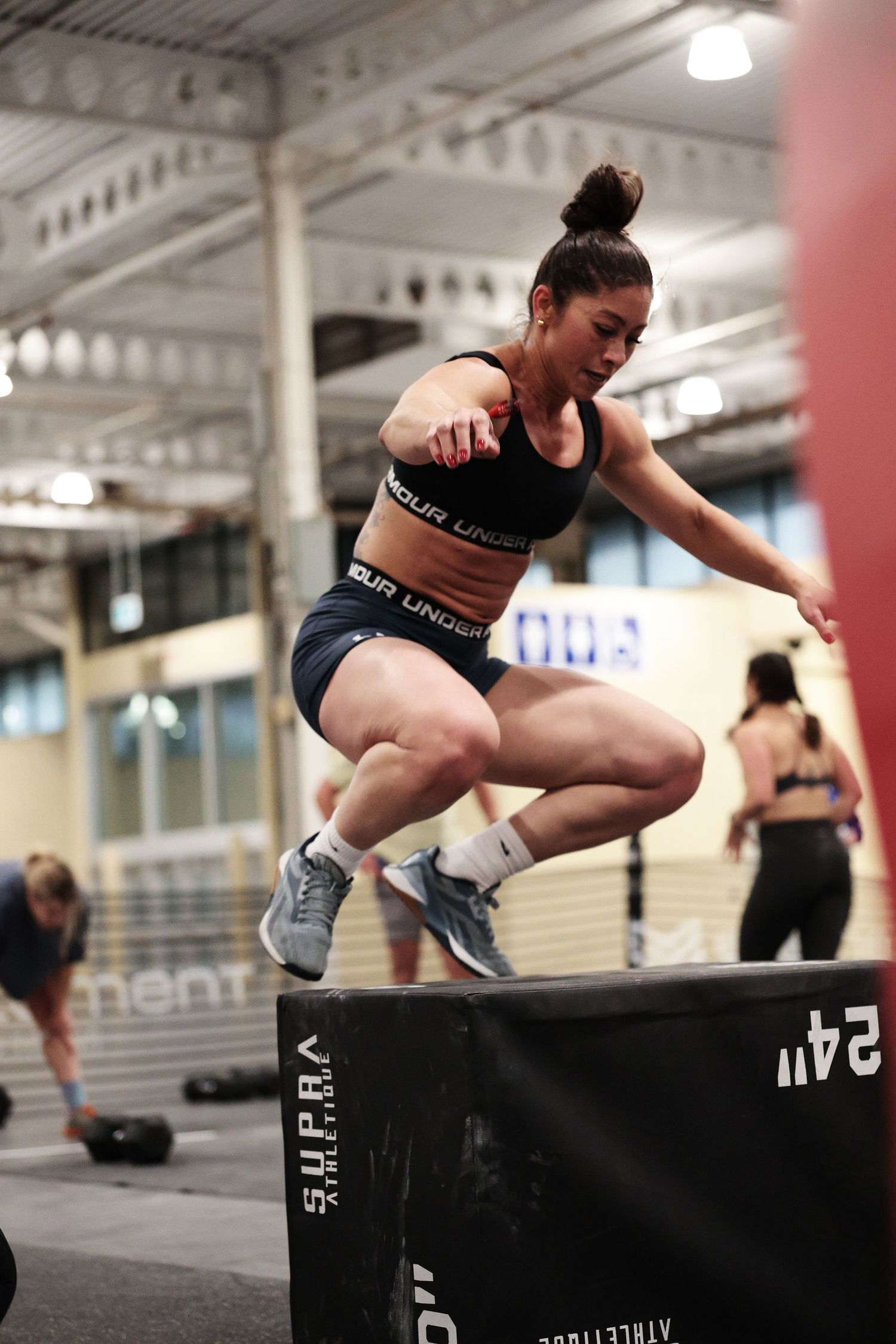 Athletic person performing a box jump exercise in a gym setting wearing black workout attire.