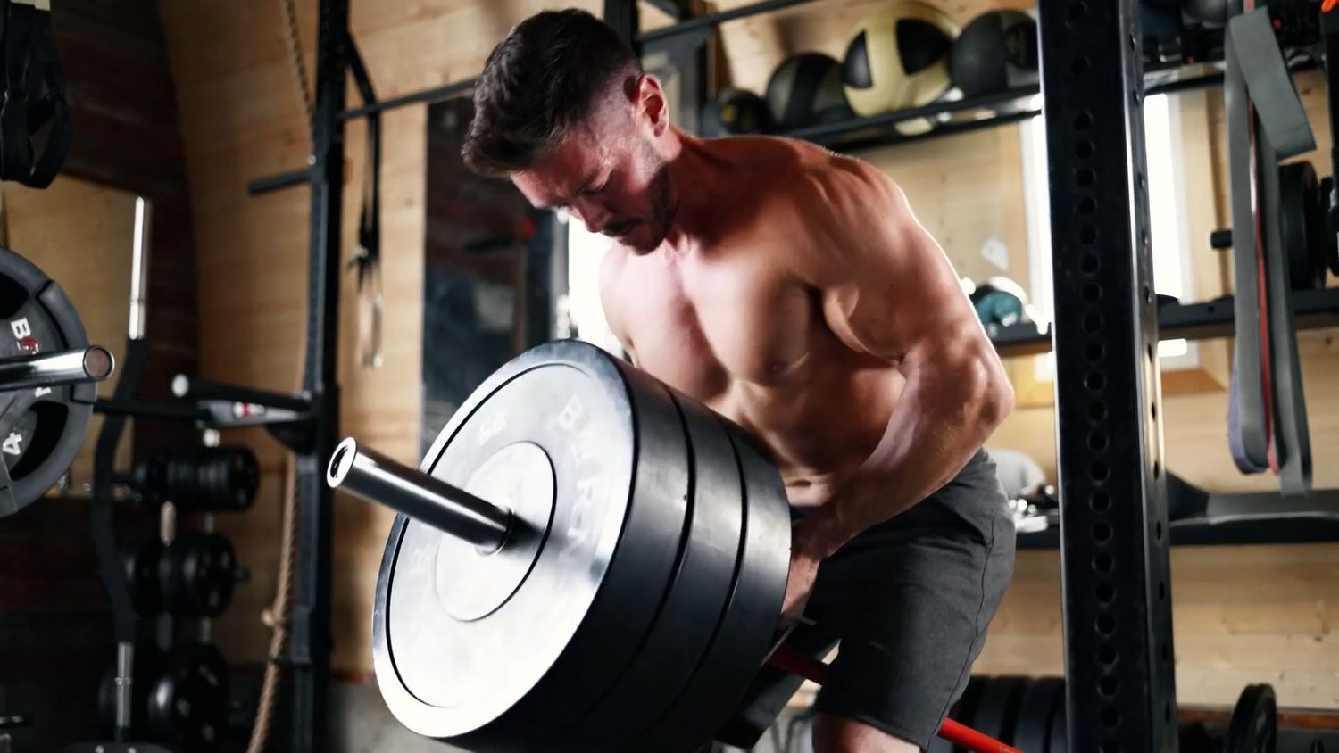 A muscular athlete performs heavy barbell rows during an intense workout session at a gym.