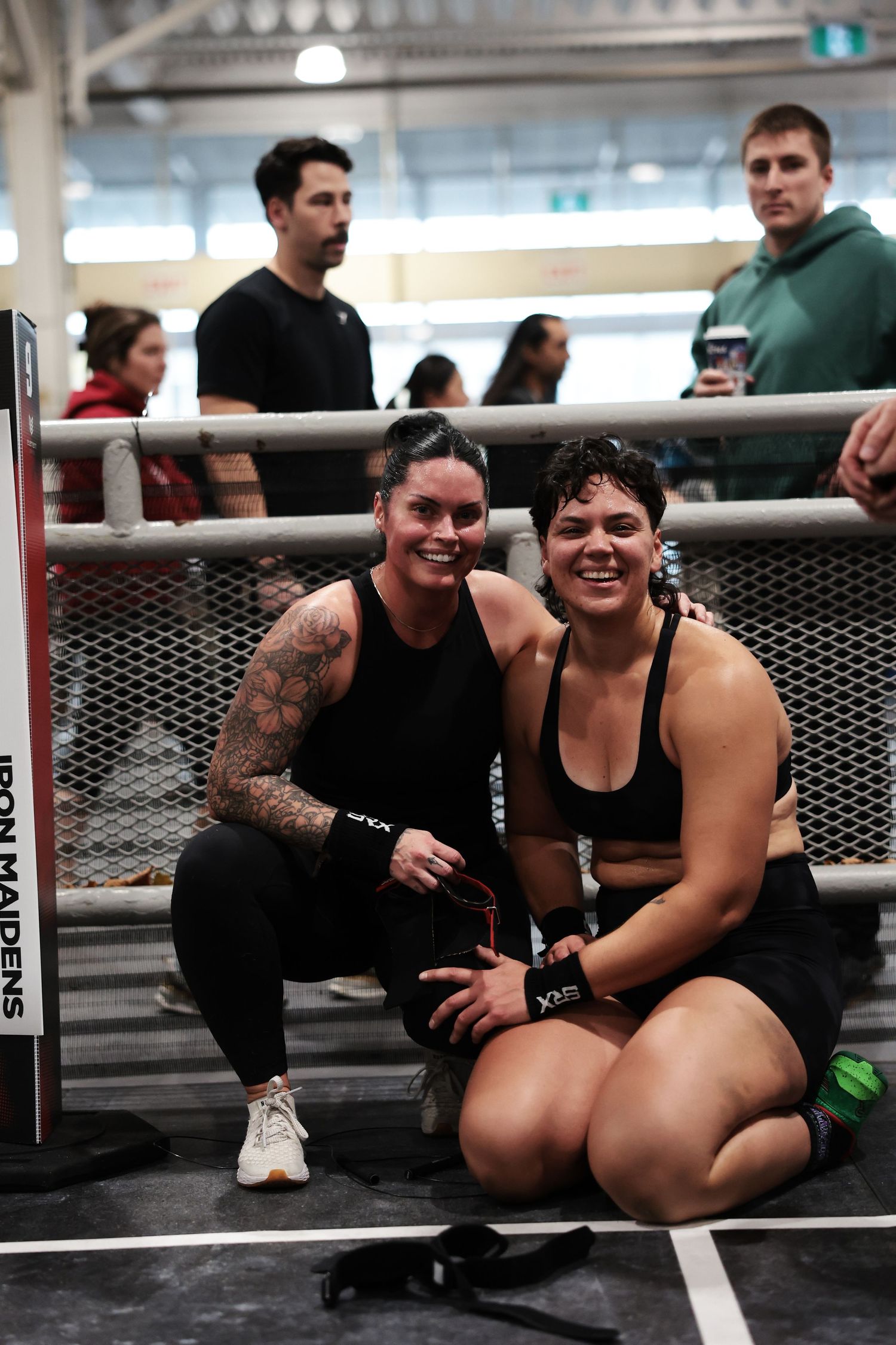 Two women posing together ringside at an Iron Maidens MMA event, smiling for the camera.